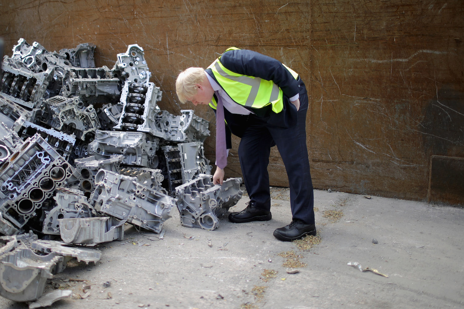 A man examines a V8 engine block in a pile of scrap.