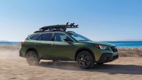 A green 2022 Subaru Outback is driving on the beach.