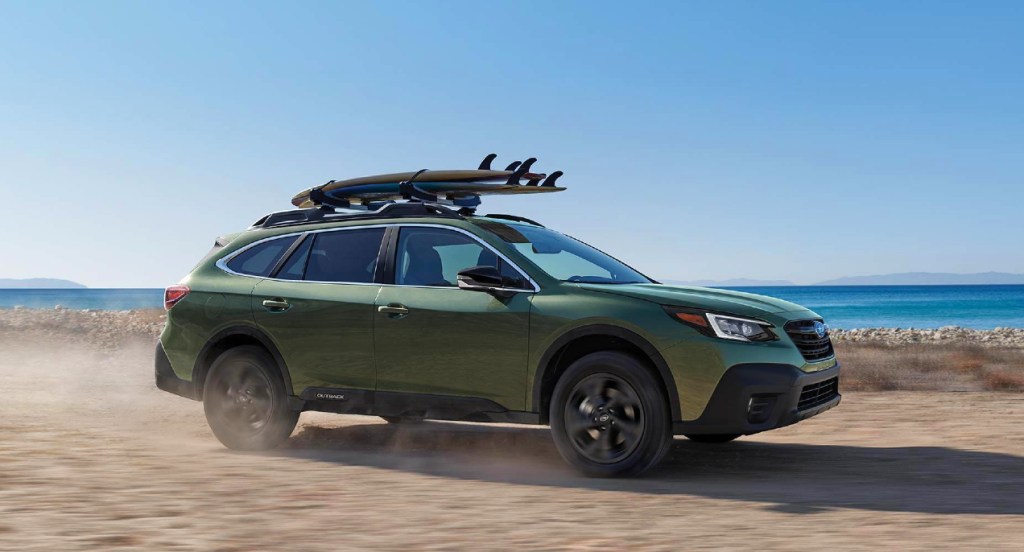 A green Subaru Outback is driving on a beach. 