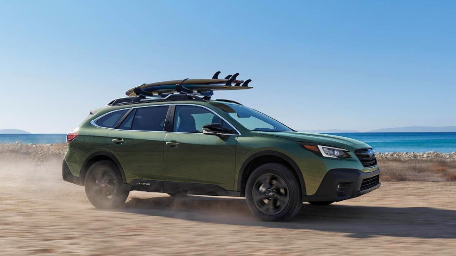A green 2022 Subaru Outback is driving on the beach.