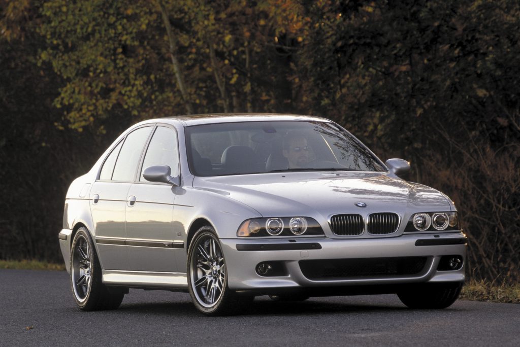 A silver E39 BMW M5 parked on a road next to a forest