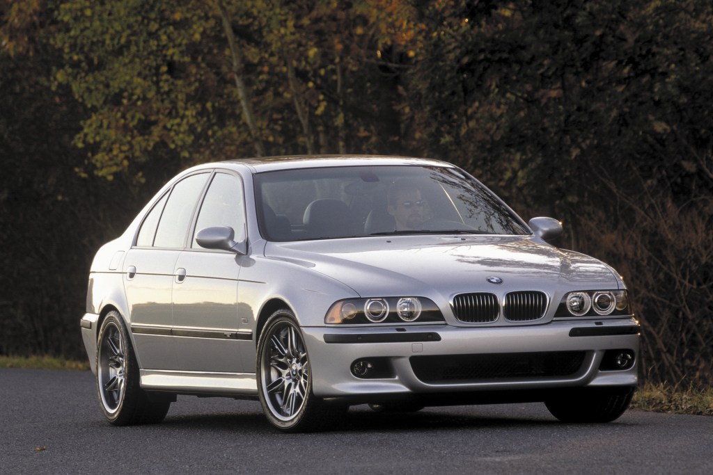 A silver E39 BMW M5 parked on a road next to a forest