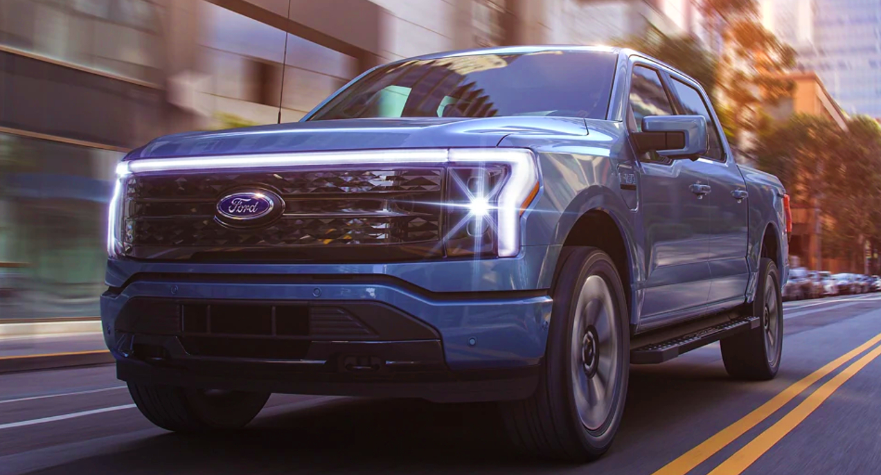 A blue 2022 Ford F-150 Lightning electric pickup truck is driving on the road.