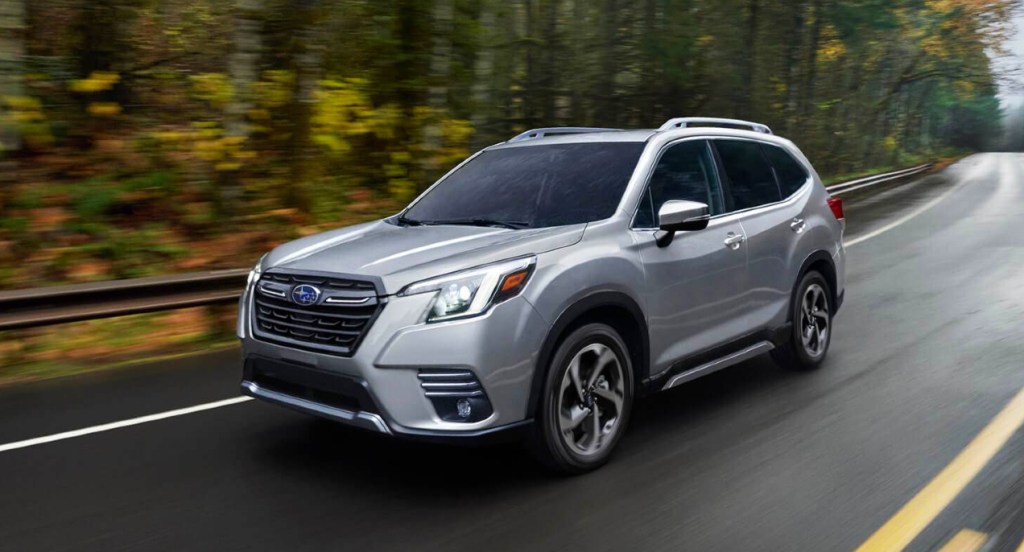 A gray Subaru Forester small SUV is driving down a wet road. 