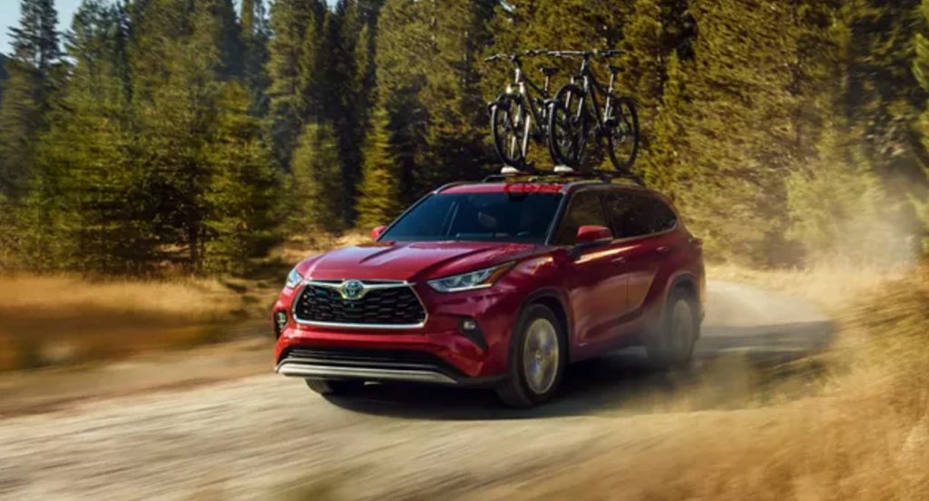 A red 2022 Toyota Highlander Hybrid midsize SUV model is driving off-road. 