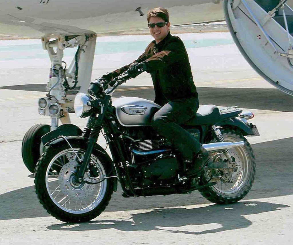 Tom Cruise on the silver MI3 Triumph Bonneville Scrambler motorcycle next to an airplane