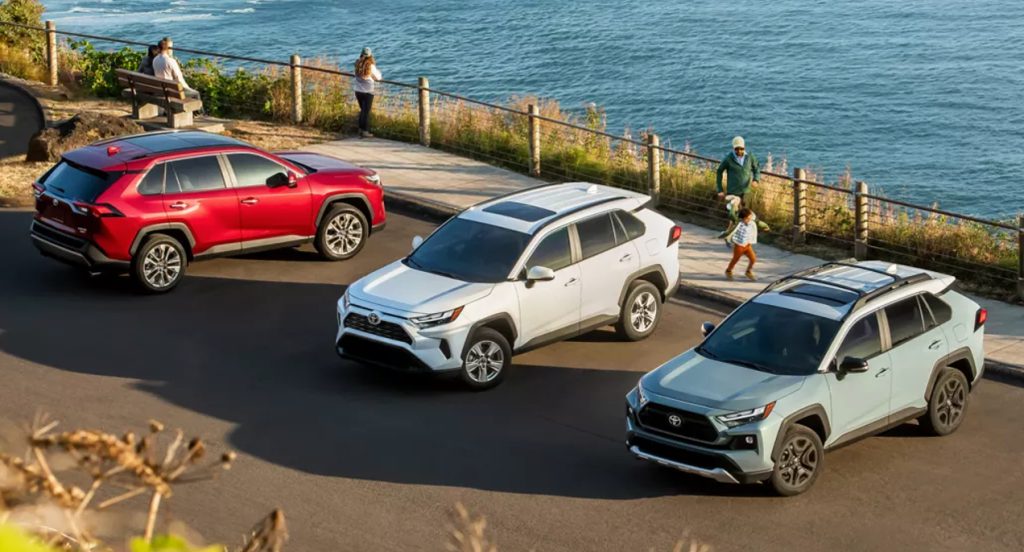A red, white, and blue Toyota RAV4 small SUV are parked near the water. 