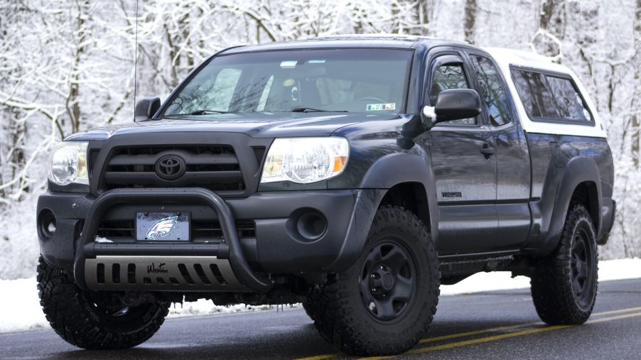 Black first generation Toyota Tacoma truck parked on a road in front of snow-covered trees.