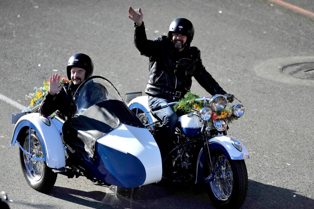 A rider on a blue-and-white vintage motorcycle carries a passenger in a matching sidecar