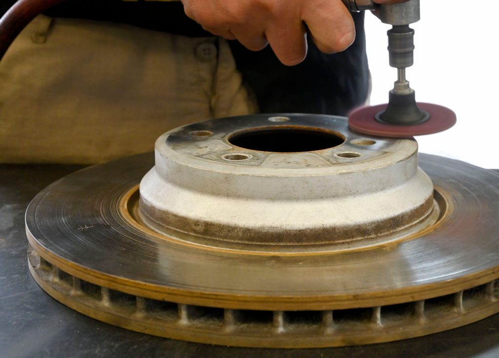 A mechanic sands down a brake disc to clean it, preventing further or future brake problems