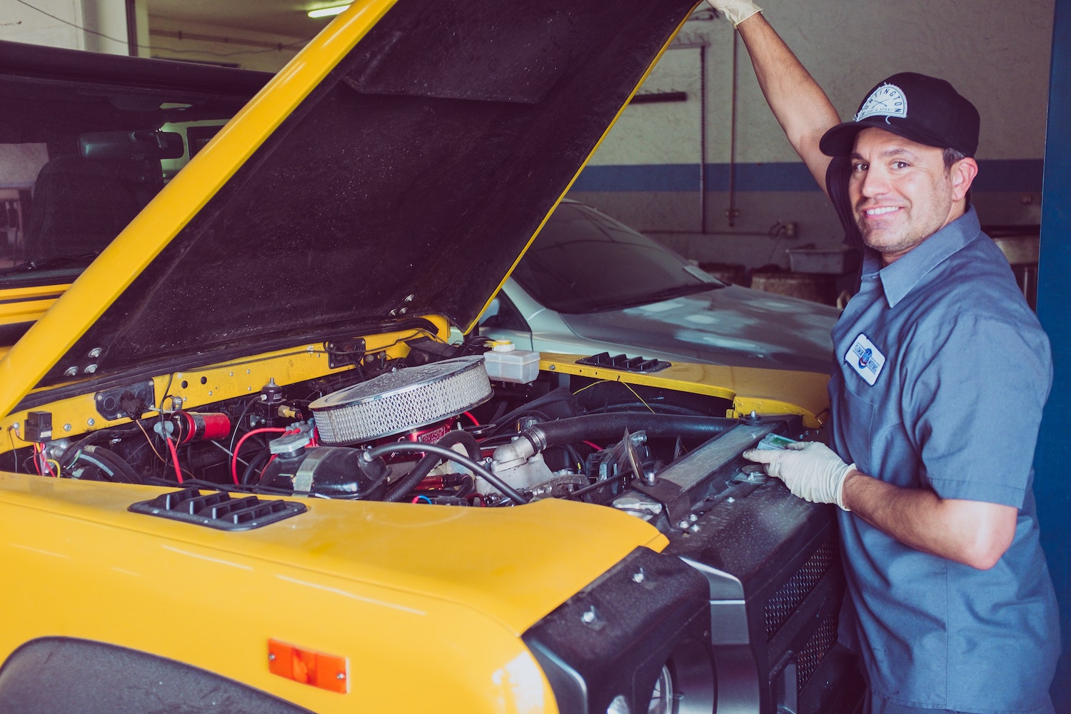 Smiling mechanic holding up the hood of a bright yellow Land Rover SUV.