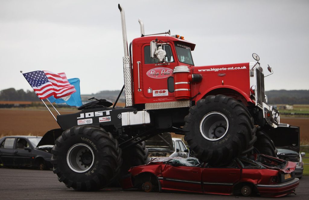 Monster truck with a huge American flag crushing a red sedan.