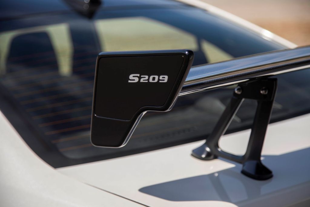 Closeup of the rear wing of the Subaru S209 STI model. The name "S209" is shown in white on a black spoiler, attached to the rear of a white Subaru STI car