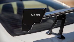 Closeup of the rear wing of the Subaru S209 STI model. The name "S209" is shown in white on a black spoiler, attached to the rear of a white Subaru STI car