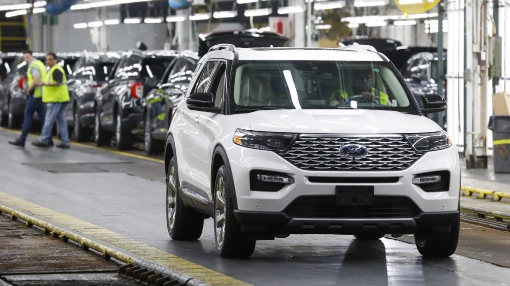 A white Ford Explorer rolls out of a manufacturing plant, driven by a mechanic