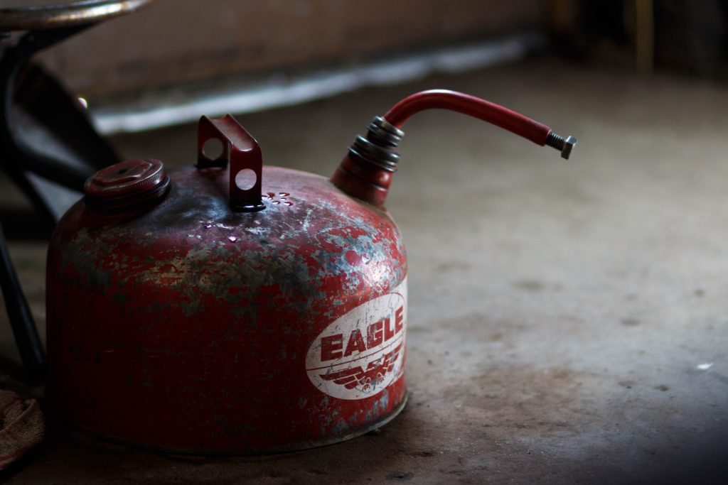An old metal gas can, its paint peeling off, sitting on a stained concrete floor.