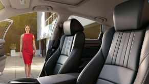 Black interior of a Honda Accord Touring with black leather seats that are heated and ventilated. The passenger-side door is open and you can see a white woman in a red dress walking toward the car