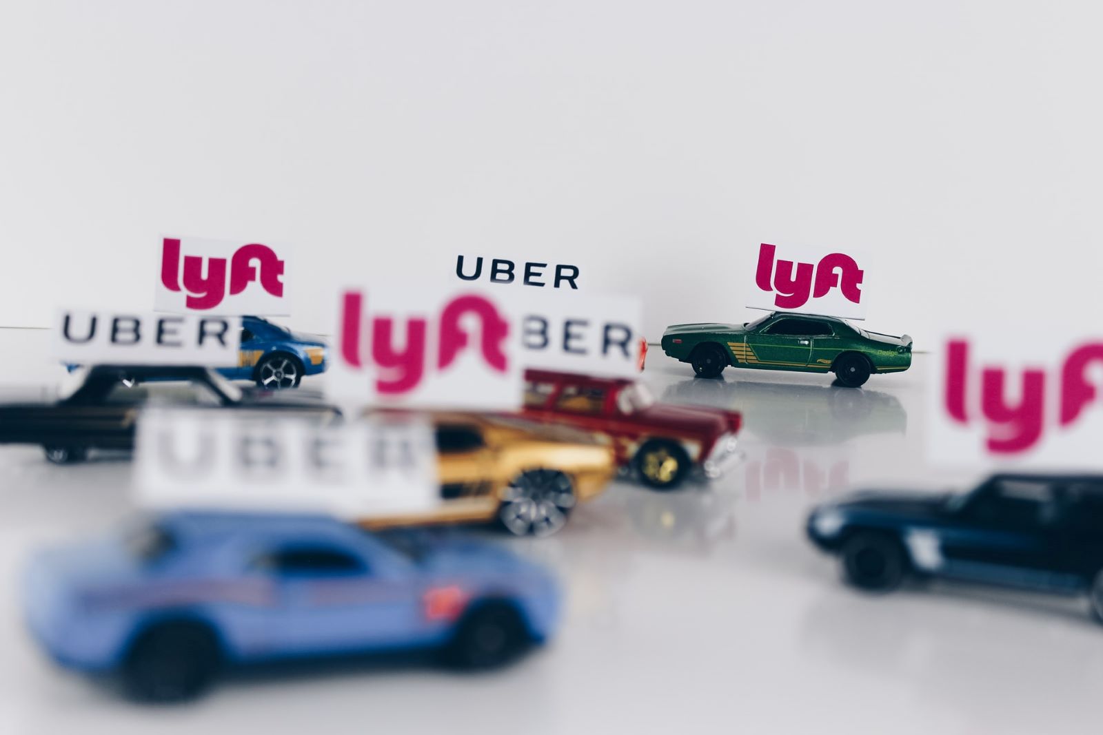 Set of toy cars collected on a flat surface. Each of the toy cars has either an Uber or Lyft sign on it