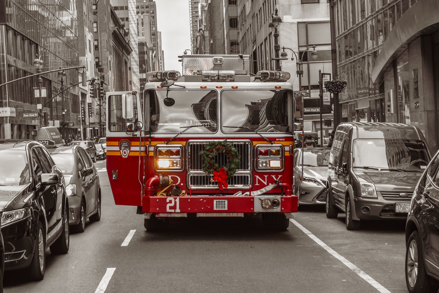 A fire truck parked between rows of cars and buildings on the streets of New York.