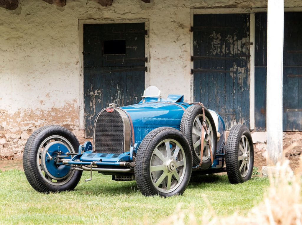 A blue 1931 Bugatti Type 51 Grand Prix race car by an old farmhouse