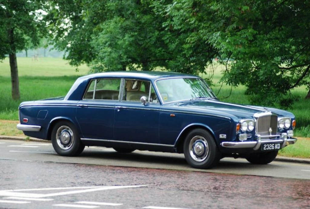 A blue 1973 Bentley T Series on a tree-lined driveway