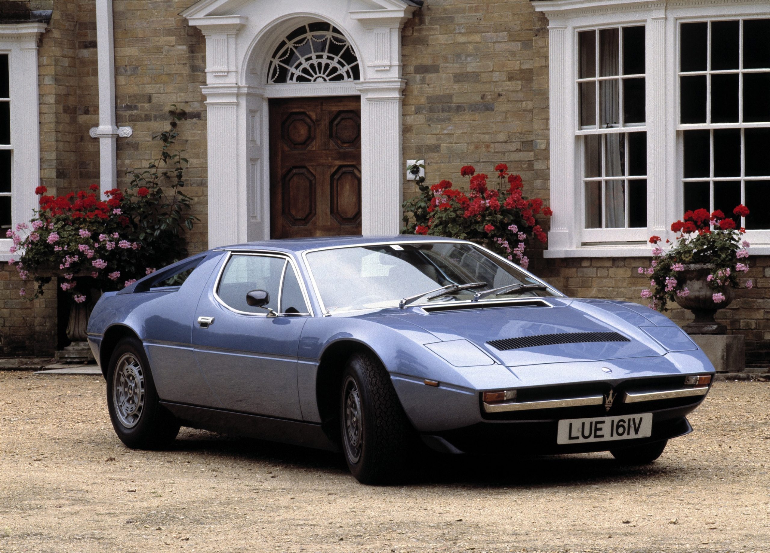 A blue 1980 Maserati Merak SS in front of a mansion