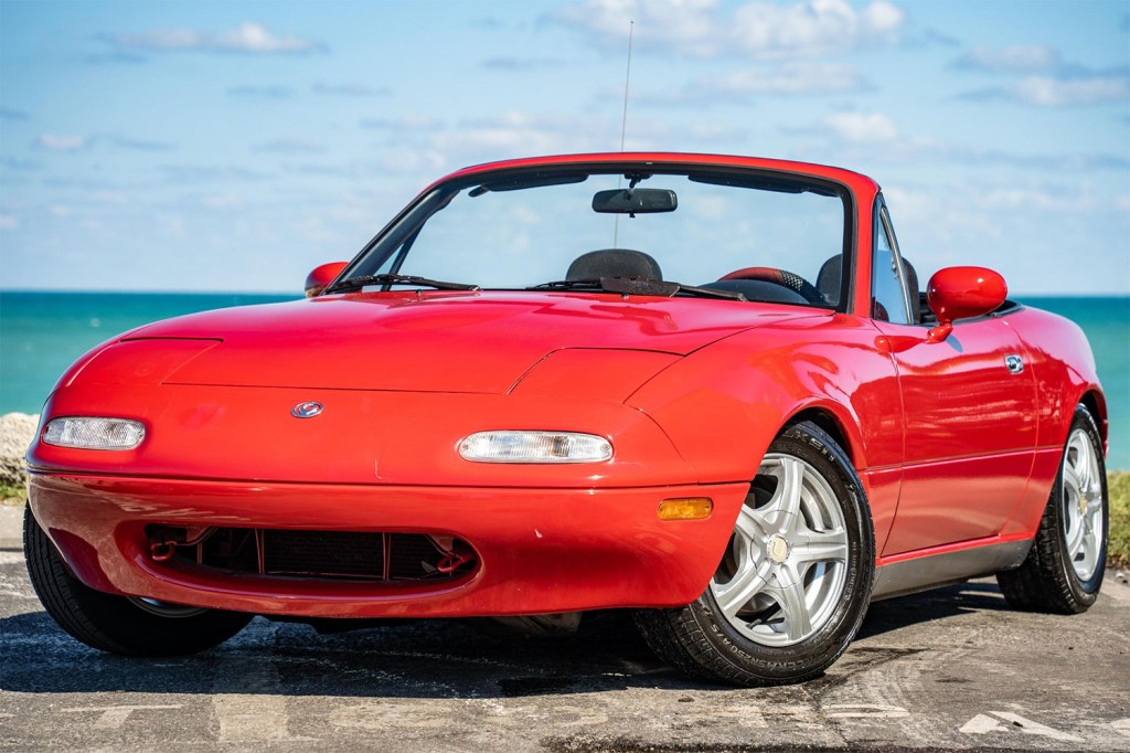 Red 1995 Mazda Miata front 3/4 with top down parked in front of ocean