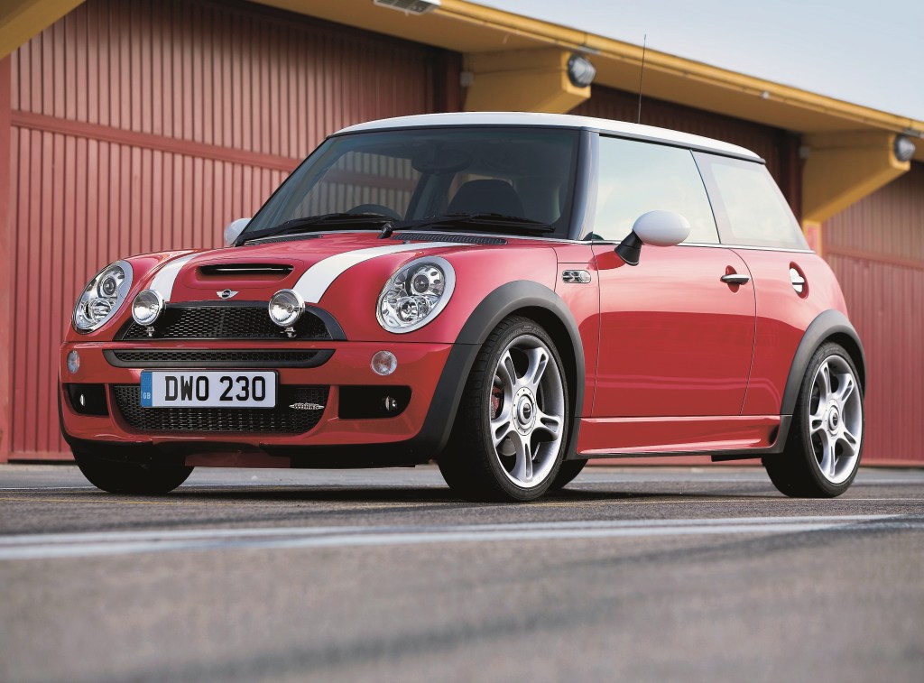 A red-with-white-stripes 2005 Mini Cooper S with JCW kit in a parking lot next to storage garages
