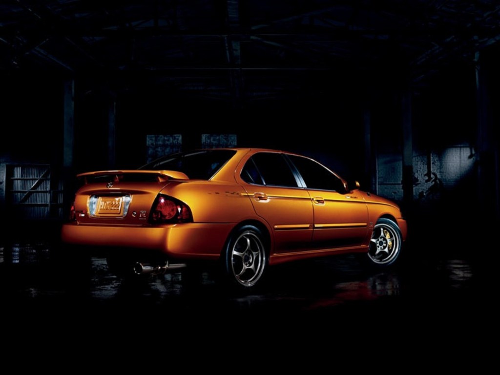The rear 3/4 view of an orange 2006 Nissan Sentra SE-R in a dark space