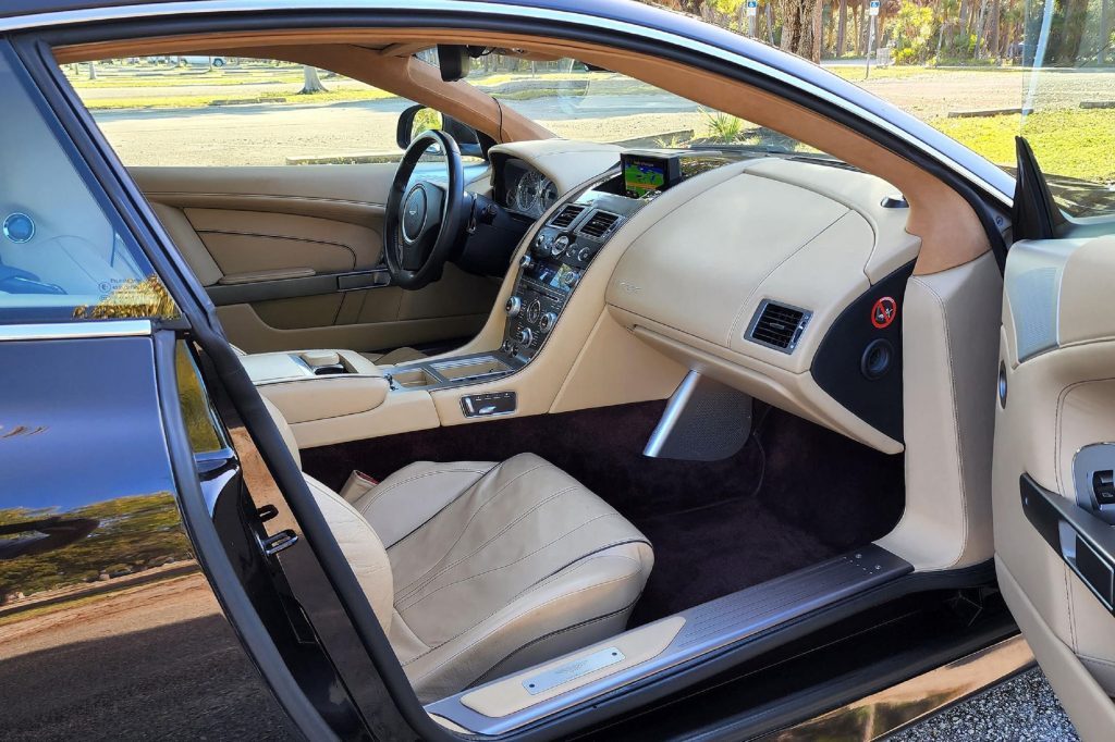 The tan-leather-upholstered front seats and dashboard of a brown 2012 Aston Martin Virage in a Florida park parking lot