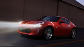 A red 2013 Nissan 370Z drives through the night with its sleek headlights lighting the road ahead.