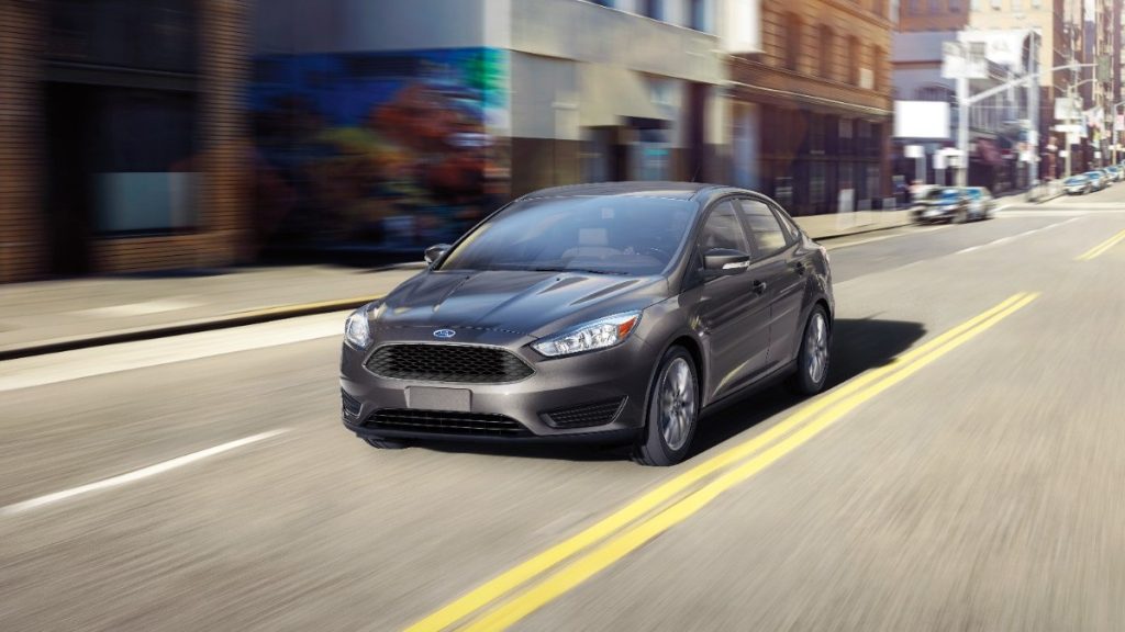 A 2016 Ford Focus SE in grey driving down a city steet basked in sunlight