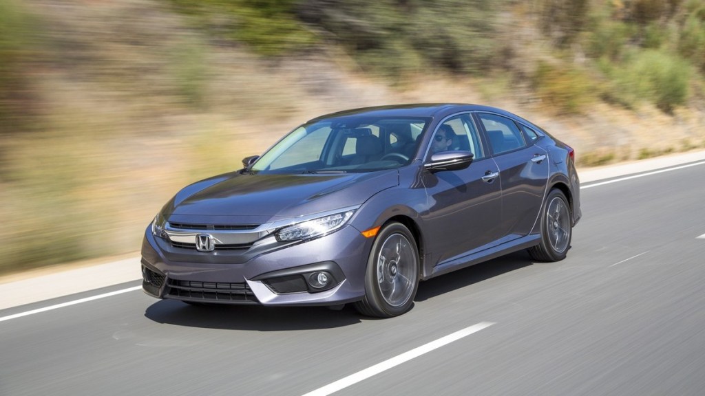 A grey 2016 Honda Civic is driving along a road next to a dirt hill