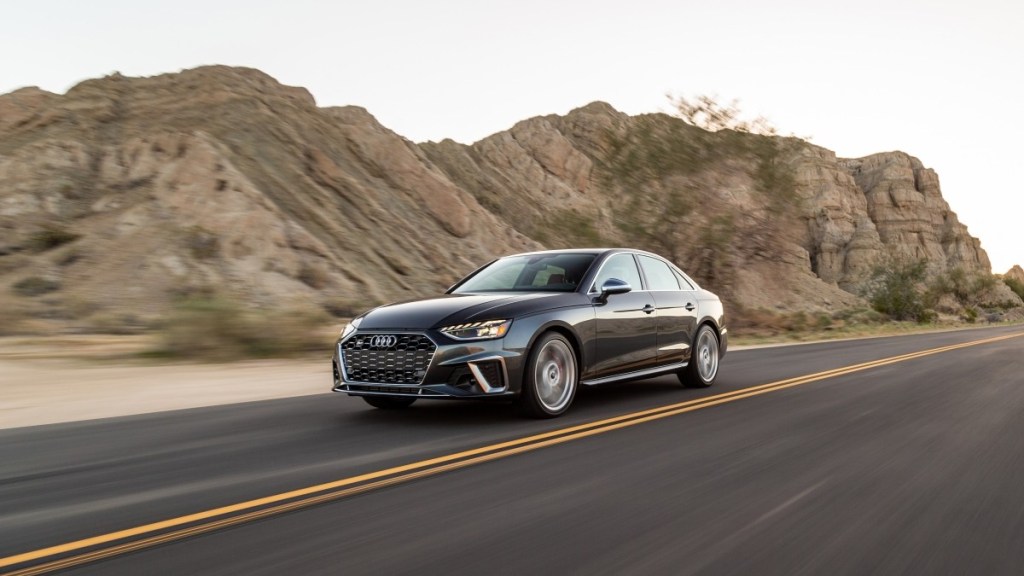  A gray 2020 Audi S4 is sown driving along a road lined by large cliffs.