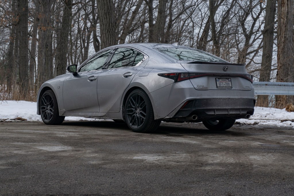 The rear 3/4 view of a silver 2021 Lexus IS 350 F Sport AWD with Dynamic Handling Package next to a snowy forest