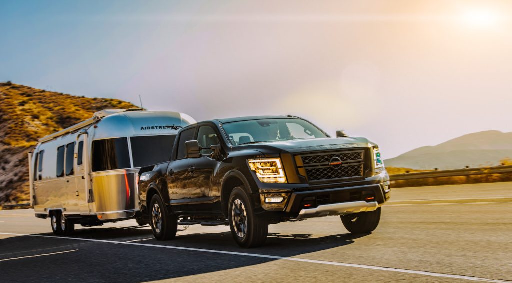 2021 Nissan Titan pickup truck pulling an airstream trailer up a mountain road in the desert.