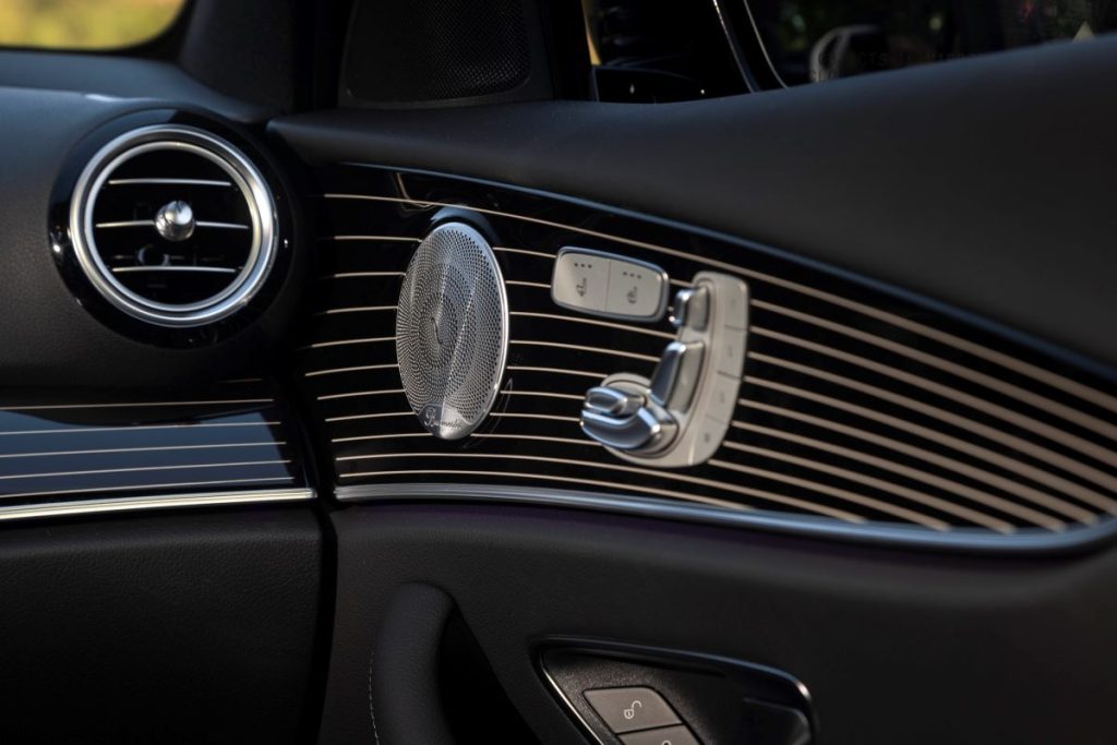 Close-up shot of the interior passenger-side door of a 2021 Mercedes-Benz E-Class, showing an artistic silver speaker and a multi-way power seat control pad