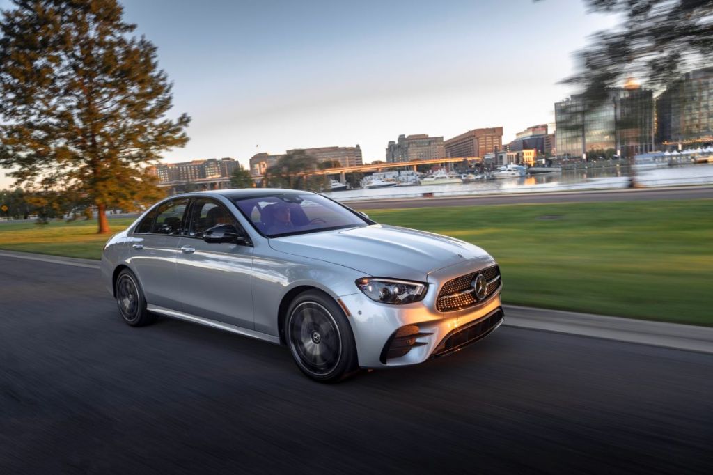 Silver Mercedes-Benz E-Class Sedan driving along a smooth road in a city, alongside a small pond
