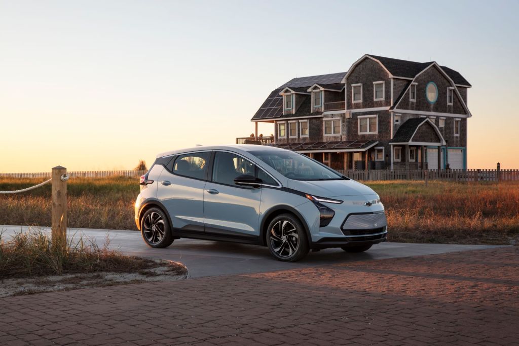 A silver 2022 Chevrolet Bolt in front of a large house. 