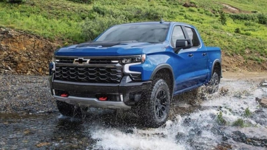 Here's a blue 2022 Chevy Silverado 1500 pickup truck splashing through a shallow creek.