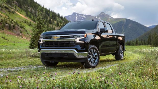 2022 Chevy Silverado LT full-size pickup truck parked on a grass field near forest mountains
