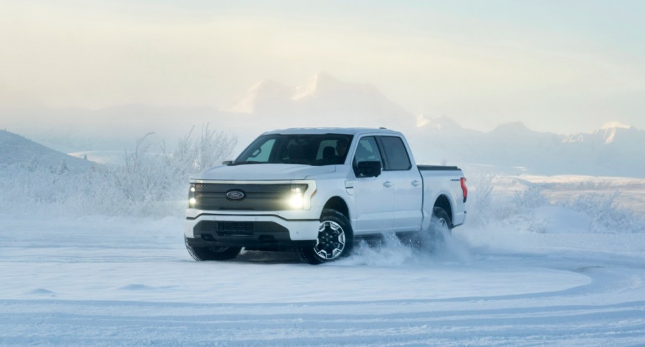 A white 2022 Ford F-150 Lightning electric pickup truck is driving in the snow.