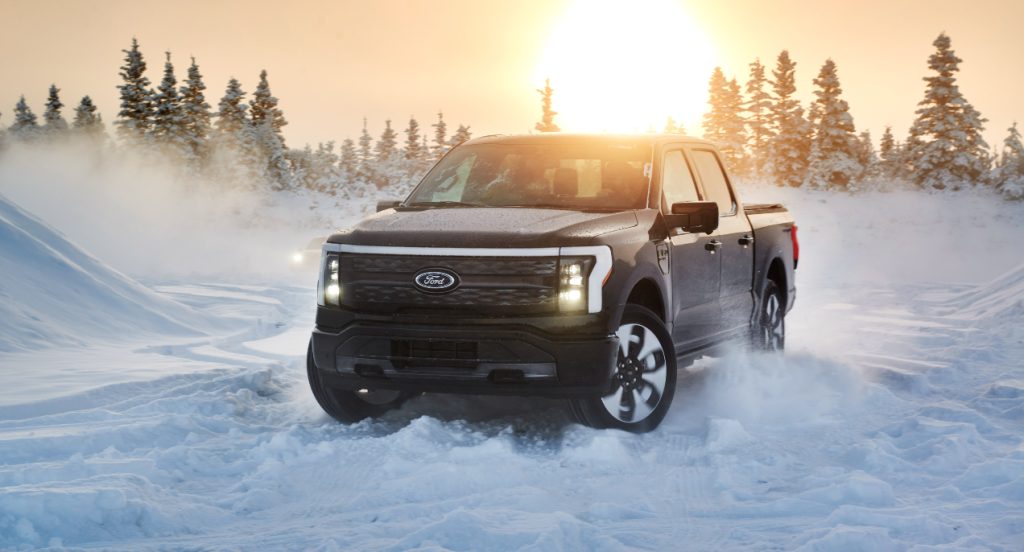 A black 2022 Ford F-150 Lightning electric pickup truck is driving in the snow. 