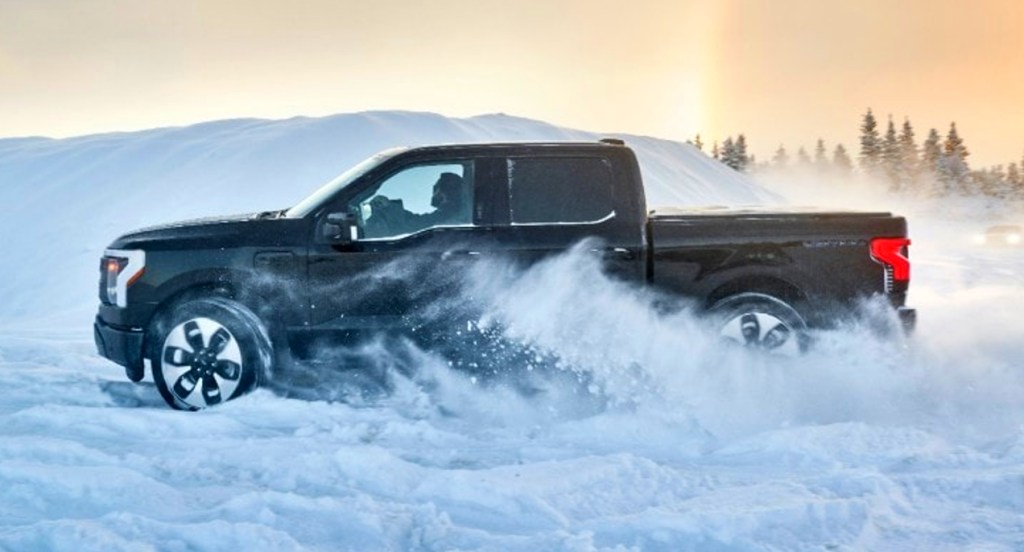 A black 2022 Ford F-150 Lightning electric pickup truck is driving through the snow. 