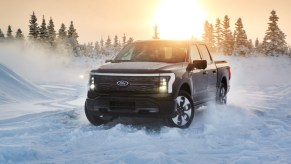 A black 2022 Ford F-150 Lightning electric pickup truck is driving in the snow.