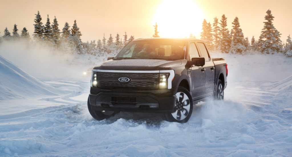 A black 2022 Ford F-150 Lightning electric pickup truck is driving in the snow.