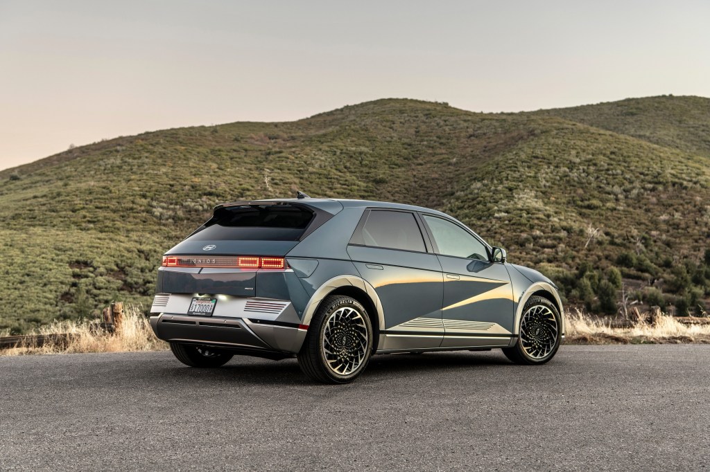 The rear 3/4 view of a blue-and-silver 2022 Hyundai Ioniq 5 by a grassy hill