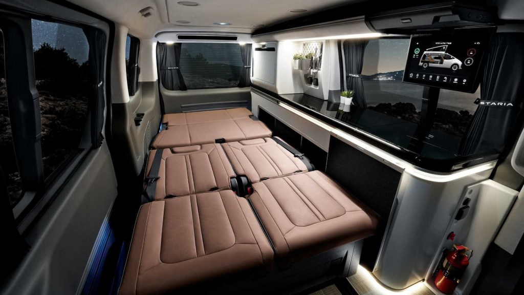 The 2022 Hyundai Staria Lounge Camper 4 interior with brown-leather folding seats and white countertop with sink, fridge, and touchscreen