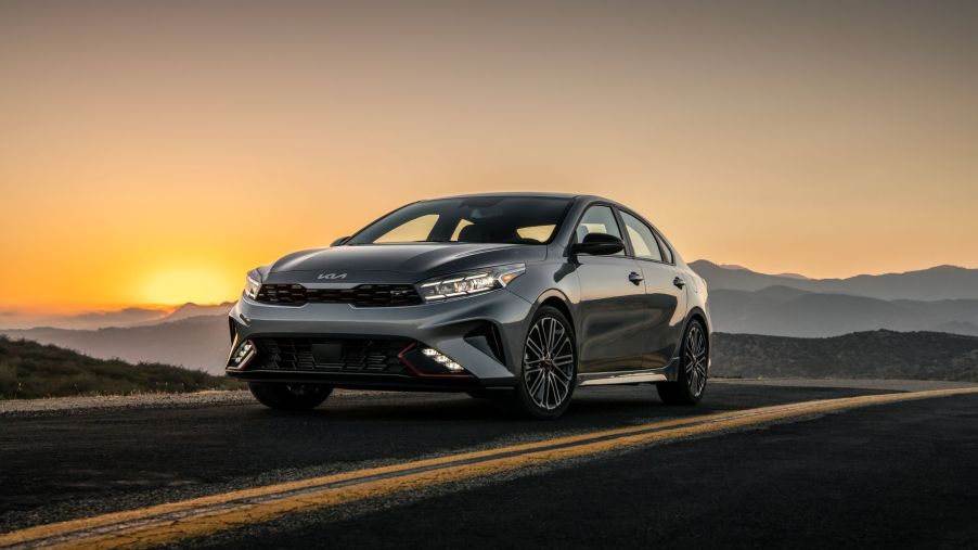 The 2022 Kia Forte GT compact sedan model in gray parked on a deserted highway stretch at sunset