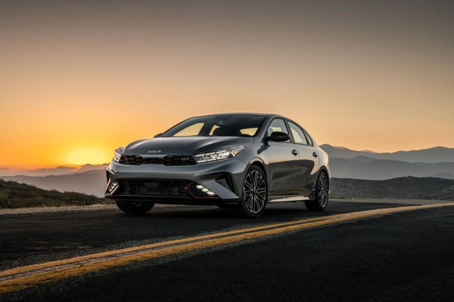The 2022 Kia Forte GT compact sedan model in gray parked on a deserted highway stretch at sunset